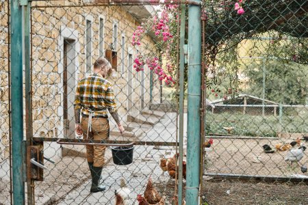 appealing hard working man with tattoos feeding chickens in their aviary while on his farm