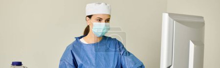 Photo for A woman in scrubs and face mask working at a computer. - Royalty Free Image