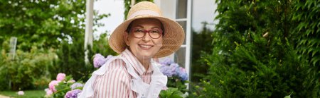 attractive cheerful mature woman with hat taking care of her hydrangea and smiling at camera, banner