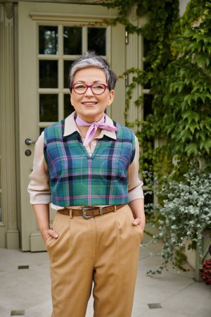 good looking debonair woman with glasses posing with hands in pockets and smiling at camera