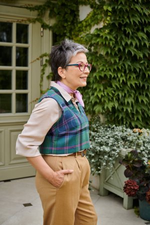 cheerful beautiful debonair woman with glasses posing with hands in pockets and looking away