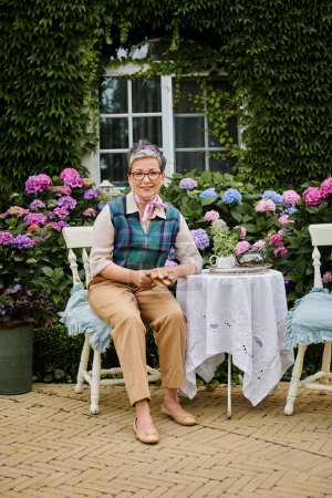 femme mûre gaie assise dans le jardin à l'heure du thé près de la maison en Angleterre et regardant la caméra