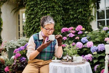 hermosa mujer madura alegre beber té caliente en el desayuno en el jardín de su casa en Inglaterra