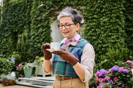 attrayant joyeuse femme mûre boire du thé chaud au petit déjeuner dans le jardin de sa maison en Angleterre