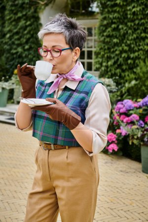 attractive joyful mature woman drinking hot tea at breakfast in garden of her house in England