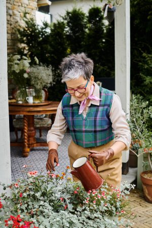 Téléchargez les photos : Attrayant joyeux mature femme en tenue chic arrosant ses fleurs près de sa maison en Angleterre - en image libre de droit