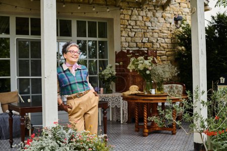 Aristokratische fröhliche reife Frau mit Brille posiert neben ihrem Haus in England und schaut weg