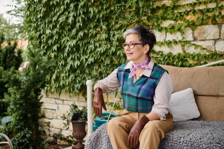 belle femme mature joyeuse assise sur le canapé près de sa maison en Angleterre et regardant loin