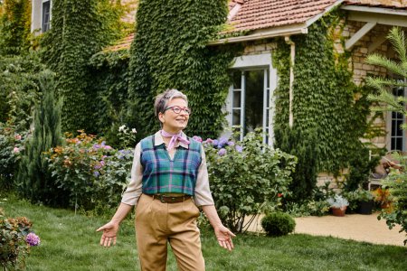 Téléchargez les photos : Élégante femme mûre joyeuse en tenue sophistiquée posant près de sa maison en Angleterre et regardant loin - en image libre de droit