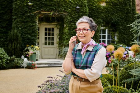 elegant cheerful mature woman with stylish glasses talking by phone net to her house in England