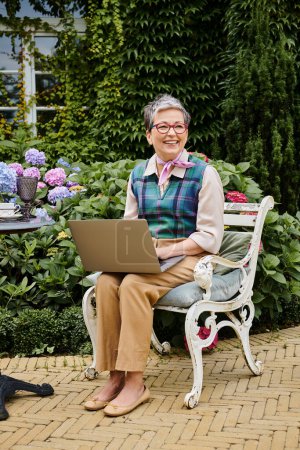debonair madura feliz mujer en traje elegante sentado con el ordenador portátil a la hora del té cerca de su casa en Inglaterra