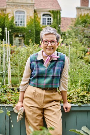 refined mature joyous woman with short hair and glasses smiling at camera near her house in England