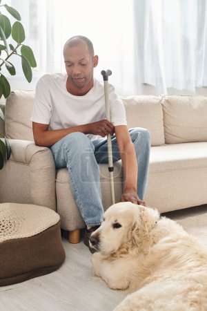 An African American man with myasthenia gravis sitting comfortably on a couch beside his loyal Labrador dog.