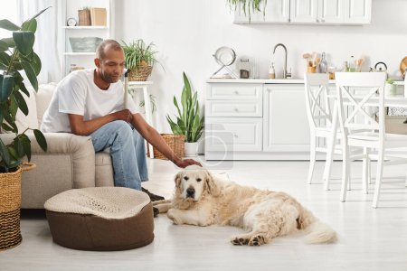 An African American man with myasthenia gravis sits beside his Labrador dog on the couch at home.