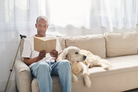 An African American man with myasthenia gravis is sitting on a couch with his Labrador dog, engrossed in reading a book.