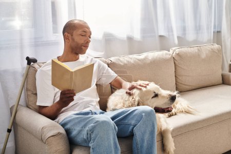 A disabled African American man with myasthenia gravis reading a book on a couch next to his loyal Labrador dog.