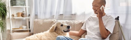 Téléchargez les photos : Un homme atteint de myasthénie grave est assis sur un canapé et parle sur un téléphone cellulaire à côté de son fidèle chien Labrador.. - en image libre de droit