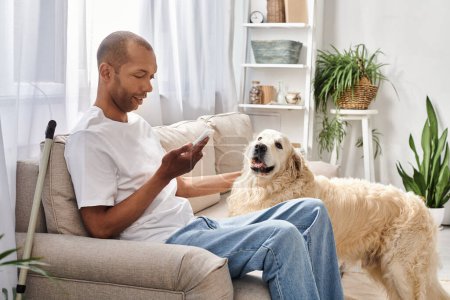 Un hombre afroamericano con miastenia gravis se sienta en un sofá, cerca de su perro Labrador y usando un teléfono inteligente