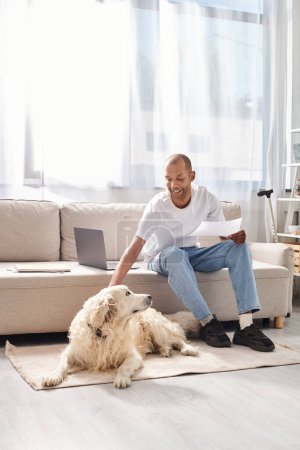 An African American man with myasthenia gravis sitting on a couch next to his loyal Labrador dog at home.