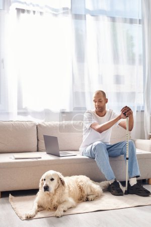 Téléchargez les photos : Un Afro-Américain handicapé se détend à côté de son fidèle chien Labrador sur un canapé confortable, embrassant la diversité et l'inclusion. - en image libre de droit