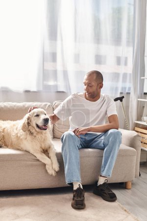 An African American man with myasthenia gravis sits on a couch next to his loyal Labrador dog in a diverse and inclusive setting.