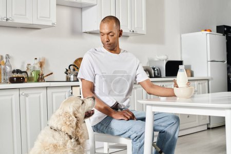 An African American man, disabled, sits at a kitchen table with his loyal Labrador dog, showcasing diversity and inclusion.