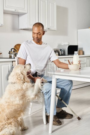 Foto de Una escena diversa e inclusiva con un hombre afroamericano sentado en una mesa con dos perros labradores. - Imagen libre de derechos