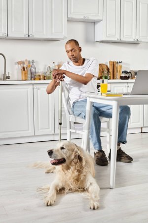 A disabled African American man sits at a table with a Labrador dog in front of him, displaying diversity and inclusion.