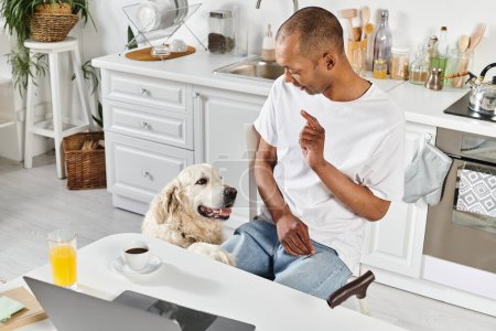 Ein Afroamerikaner mit Behinderung und sein Labrador Retriever genießen einen gemeinsamen Moment in einer gemütlichen Küche.