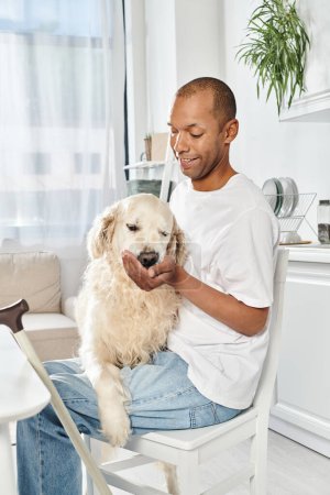 Ein behinderter Afroamerikaner sitzt auf einem Stuhl und wiegt friedlich einen Labrador-Hund in seinen Armen.