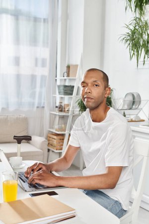 Ein Mann afroamerikanischer Abstammung, der mit Myasthenia gravis lebt, benutzt an einem Tisch einen Laptop.