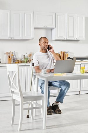Un hombre afroamericano discapacitado con síndrome de Miastenia Gravis sentado en una mesa de la cocina, profundamente involucrado en una llamada telefónica.