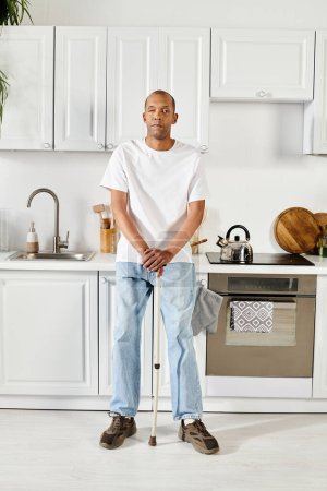 Un hombre afroamericano con un bastón se para con confianza en una cocina, mostrando fuerza y resiliencia.