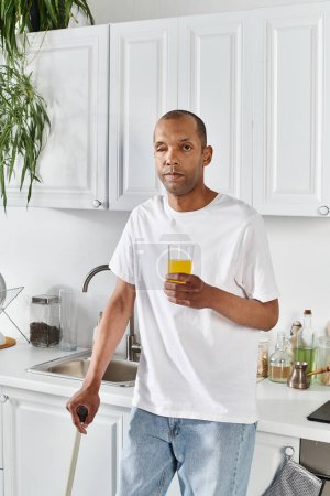 An African American man with myasthenia gravis syndrome stands in a kitchen holding a glass of orange juice.