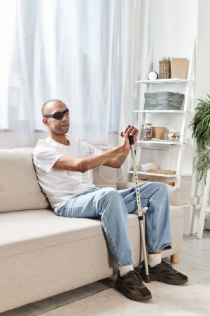 Hombre afroamericano con síndrome de miastenia gravis sentado en un sofá, sosteniendo un bastón, profundamente en el pensamiento.