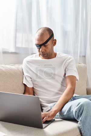 African American man with myasthenia gravis syndrome using laptop on a couch.