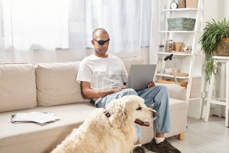 Ein Mann mit Myasthenia-gravis-Syndrom arbeitet am Laptop, während ihm ein treuer Labrador-Hund auf der Couch Gesellschaft leistet.
