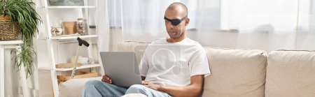 Ein afroamerikanischer Mann mit Myasthenia-Gravis-Syndrom sitzt mit seinem Labrador-Hund in der Nähe auf einer Couch und benutzt einen Laptop..
