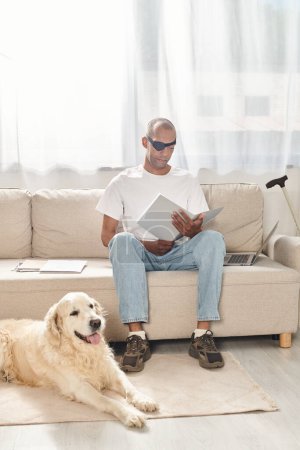 A disabled African American man with myasthenia gravis syndrome sitting on a couch next to a Labrador dog, embodying diversity and inclusion.