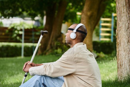 Ein afroamerikanischer Mann mit Myasthenia-Gravis-Syndrom sitzt mit Kopfhörern im Gras und genießt Musik.