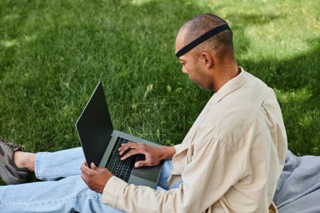 A disabled African American man with myasthenia gravis syndrome, working on a laptop while sitting on green grass