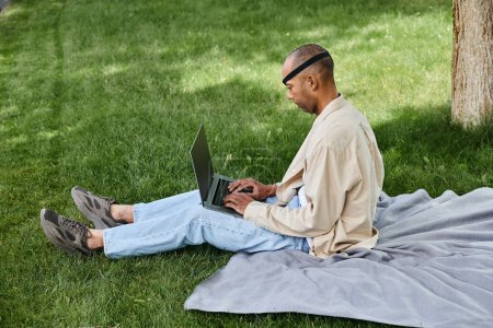 Photo for African American man with Myasthenia Gravis in a wheelchair, using a laptop outside on grass - Royalty Free Image