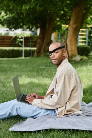 Ein afroamerikanischer Mann mit Myasthenia gravis benutzt einen Laptop, während er auf Gras sitzt