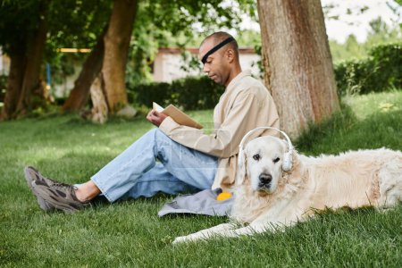 An African American man with a disability sits in the grass with his Labrador dog, embodying diversity and inclusion.