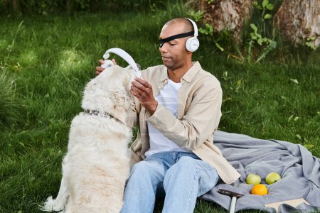 African American man with myasthenia gravis sitting on a blanket, enjoying music with Labrador dog wearing headphones.