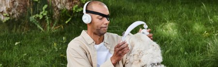 An African American man with myasthenia gravis syndrome relaxes in the grass with a Labrador dog wearing headphones.
