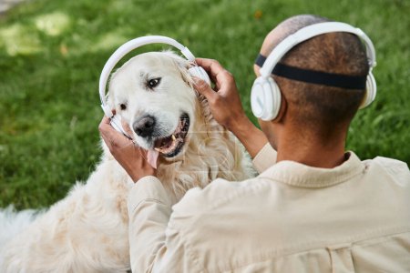 A disabled African American man listens intently to a Labrador dog wearing headphones.