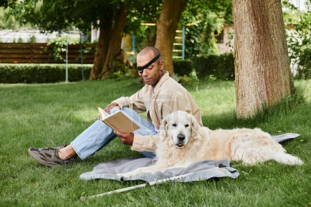 An African American man with myasthenia gravis syndrome sits in the grass with his Labrador, engrossed in a book.