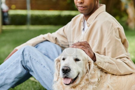 A man with myasthenia gravis syndrome peacefully sits in grass with his loyal Labrador dog by his side.