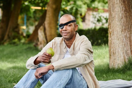 Ein behinderter Afroamerikaner sitzt friedlich auf einer Decke und hält einen Apfel in den Händen
